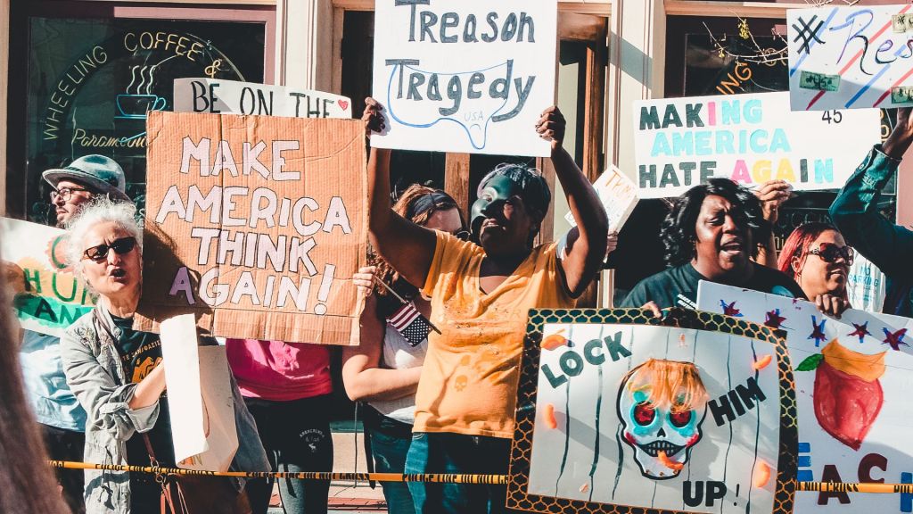 Diverse protestors holding anti-Trump signs at a political rally calling for justice and unity.